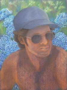 sun-kissed man in blue hat with blue hydrangeas in background on blue paper